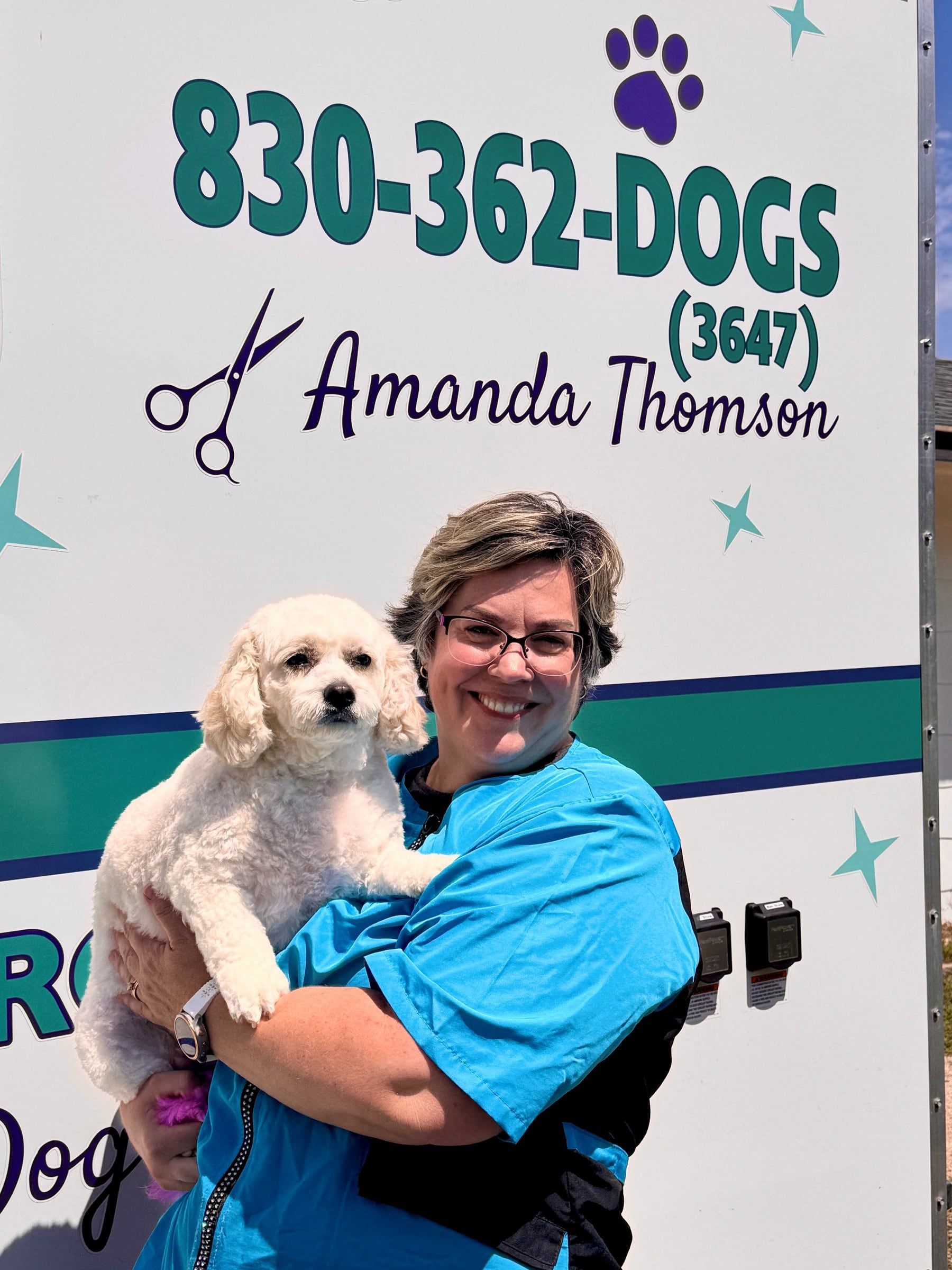 Amanda holding her small white dog Nellie Bean in front of the grooming trailer