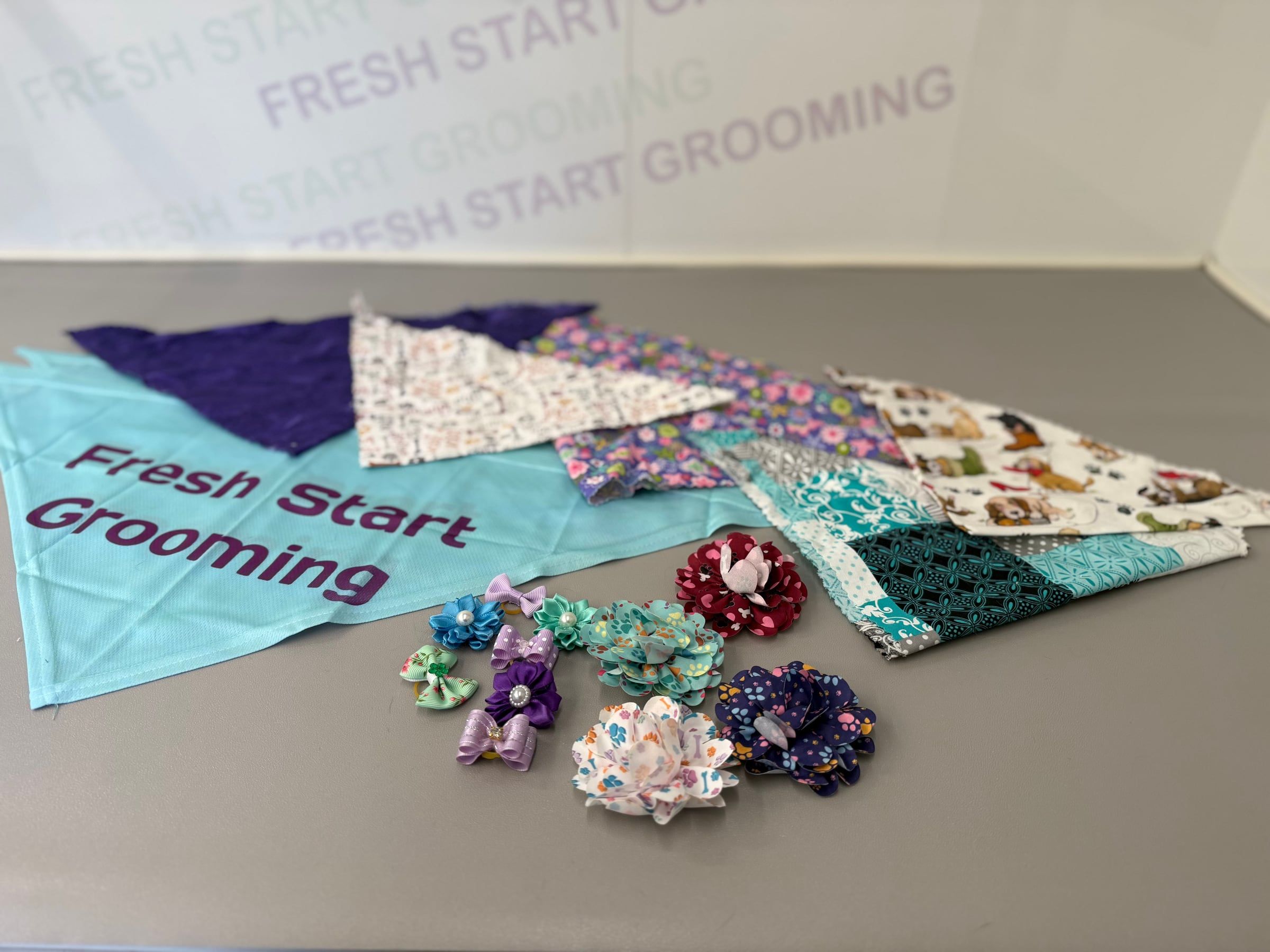 A spread of grooming bandanas and fabric bows on the grooming table, including the teal Fresh Start Grooming bandana