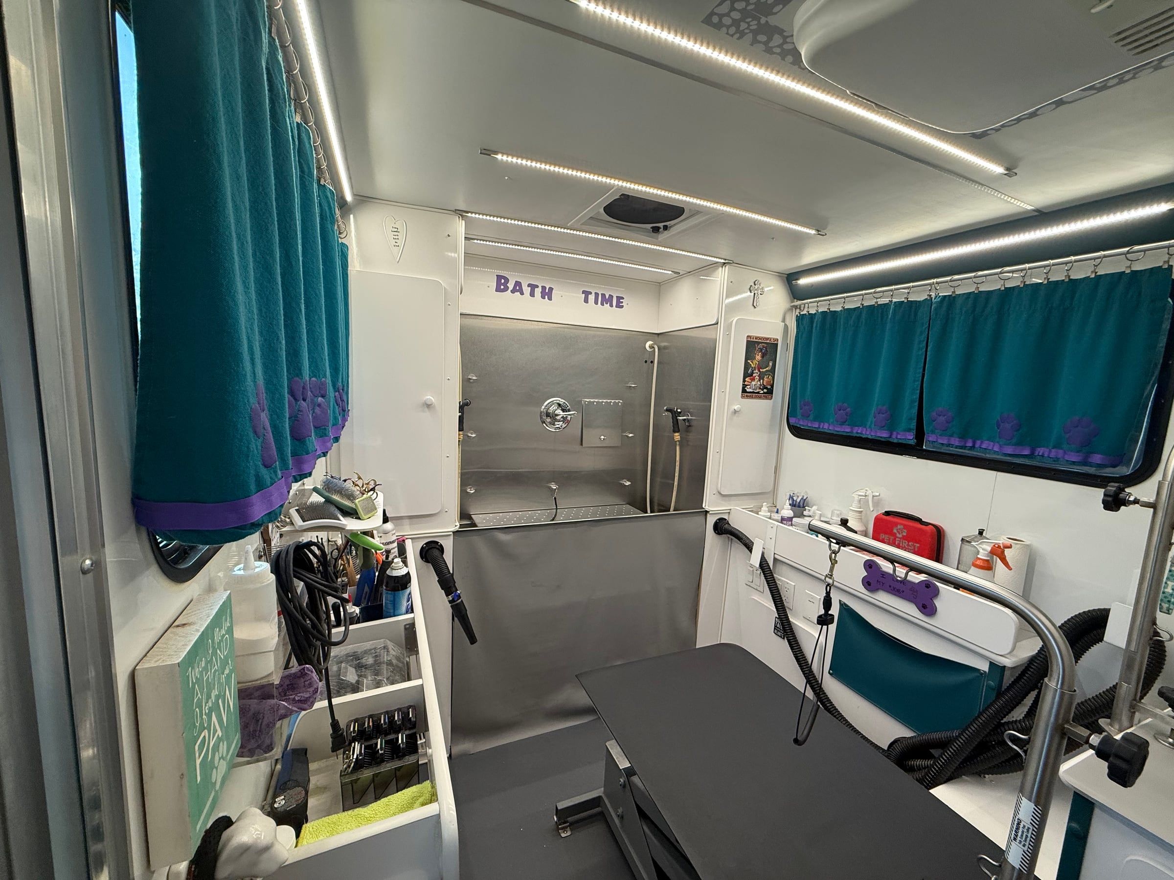 Inside the trailer: stainless steel Bath Time tub at the back, grooming table in front, teal paw-print curtains