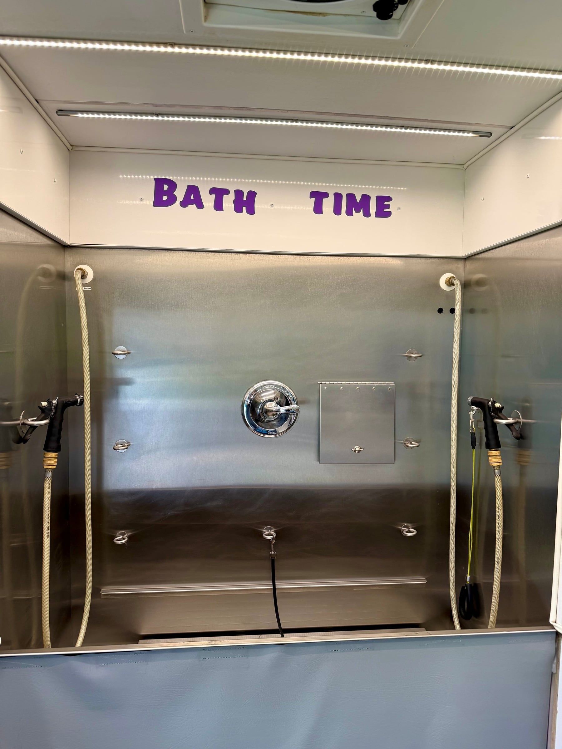 Stainless steel tub beneath the hand-lettered Bath Time sign inside the trailer